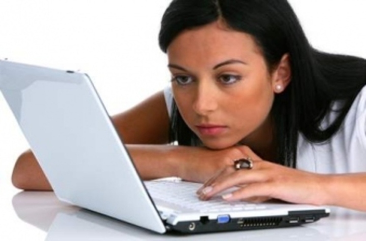 Žena s opřenou hlavou o ruku hledí do notebooku 